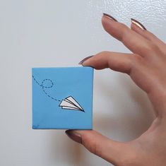 a woman's hand holding a small blue piece of paper with an airplane drawn on it