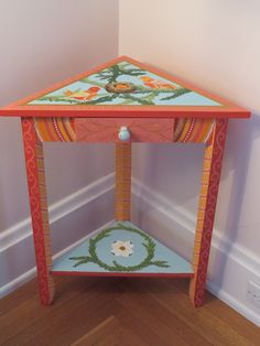 an orange and blue table sitting on top of a hard wood floor next to a white wall