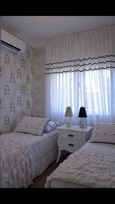 two beds in a room with curtains on the windowsill and wall paper behind them