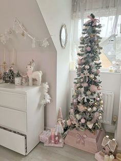 a white christmas tree in a room with pink and silver decorations on the walls, next to a chest of drawers