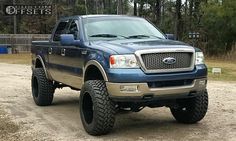 a blue pickup truck parked on top of a dirt road in front of some trees