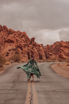 a woman is walking down the middle of an empty road in front of large rocks