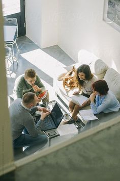 four people sitting around a table with laptops and papers on it by an open window