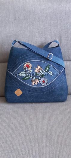 a blue purse sitting on top of a couch next to a gray sofa cushion with flowers painted on it