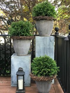 three large pots with plants in them sitting on a deck next to a lantern and fence