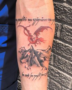 a man with a dragon tattoo on his arm next to a mountain and sky background