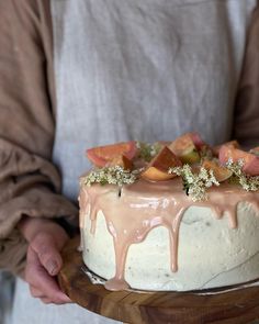 a person holding a cake with frosting and fruit on top