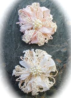 two white and pink flower brooches sitting on top of a rock