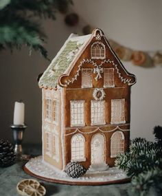 a gingerbread house decorated with icing and christmas decorations on a table next to pine cones