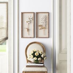 two framed pictures hang on the wall next to a chair with flowers and books in it