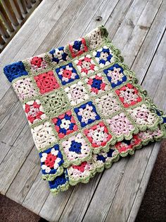 a crocheted granny blanket sitting on top of a wooden table next to a bench