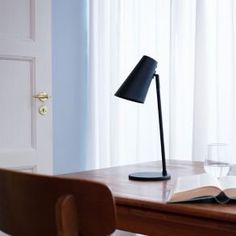 an open book on a desk next to a lamp and wine glass in front of the window