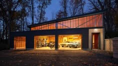 two cars are parked in the garage with their doors open at night, while another car is on the driveway