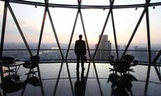 a man standing in the middle of a room with chairs and windows looking out on a city