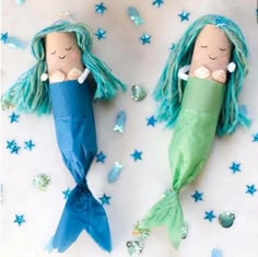 two little mermaid dolls laying on top of a bed next to blue and green stars