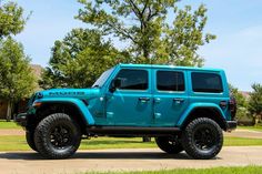 a blue jeep parked on the side of a road in front of some trees and grass