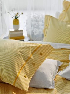 a bed with yellow and white sheets and pillows