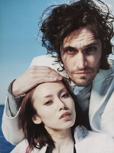 a man and woman posing for a photo in front of the ocean with their arms around each other