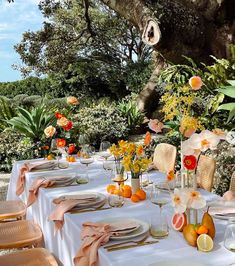 an outdoor table set up with flowers and oranges in vases on the table