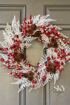 a white wreath with red berries and pine cones is hanging on the front door,