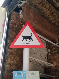 a street sign with a cat on it in front of a brick wall and ceiling