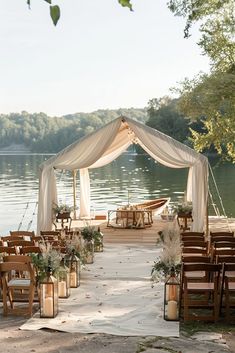 an outdoor ceremony setup with chairs and flowers on the ground next to water, surrounded by greenery