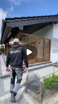 a man walking down the sidewalk in front of a building with wooden slats on it