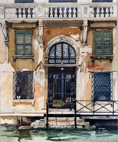 an old building with green shutters next to a body of water in front of it