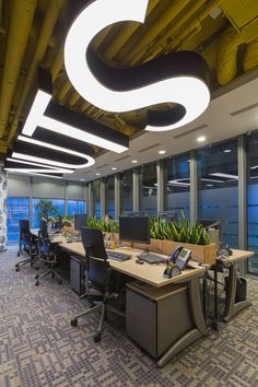 an office with two desks, computers and planters on the floor in front of large windows