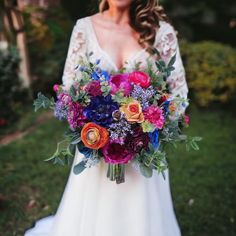 a woman holding a bouquet of flowers in her hands and wearing a white dress with lace sleeves