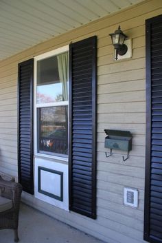 an empty chair sitting in front of a window on the side of a house with shutters open