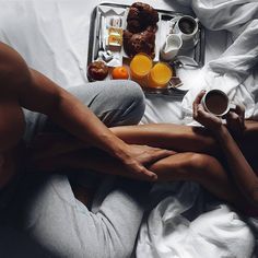 two people laying in bed next to each other with breakfast on the tray behind them