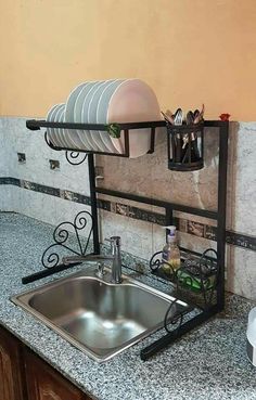 a kitchen sink sitting under a window next to a metal rack with dishes on it