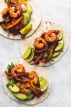 three shrimp tacos with avocado and cilantro on top, sitting on a marble surface