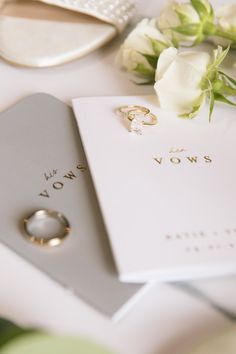 two wedding rings on top of a white card next to flowers and a ring box