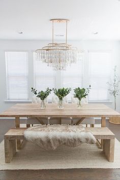 a dining room table with two benches and vases on top of it, in front of the window