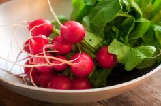 radishes and greens in a white bowl on a wooden table