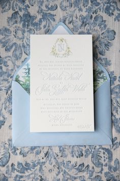 the wedding stationery is displayed on top of an envelope and in front of a blue floral wallpaper