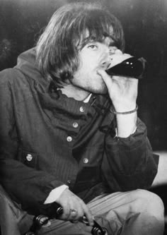 an old photo of a man drinking from a bottle while sitting in a chair with his hand on his face