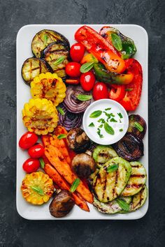 grilled vegetables on a platter with ranch dressing and fresh herbs, top view