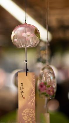 three glass ornaments hanging from strings with chinese writing on them and pink flowers in the background