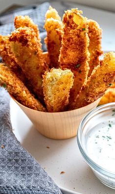 a bowl filled with fried food next to a small bowl of ranch dressing on a white plate