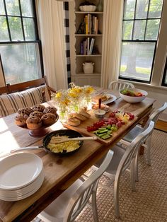 a wooden table topped with plates and bowls filled with food on top of it next to windows