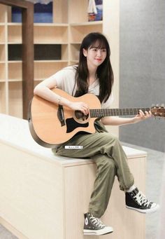 a woman sitting on top of a counter holding a guitar