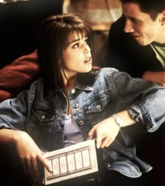 a man and woman sitting next to each other on a couch looking at an electronic device