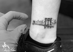 a person with a small tattoo on their ankle that has a bridge in the background