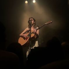 a woman holding a guitar while standing in front of a microphone on top of a stage