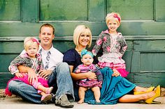 a family sitting on the ground in front of a green door with their two children