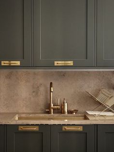 a kitchen with gray cabinets and gold pulls on the handles, brass faucet