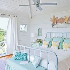 a bedroom with white walls and wood floors has a large bed in the center, along with two windows that look out onto the ocean